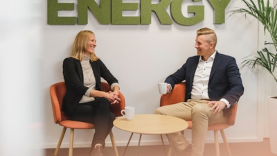 Employees Minna Lindholm and Arto Peltola sitting down in front of sign on the wall reading "energy"