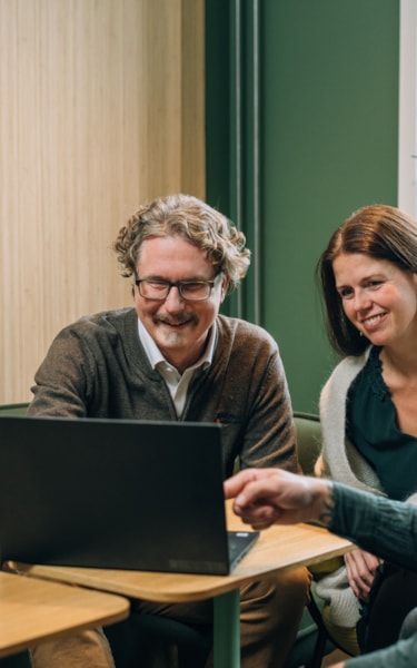 Four employees, two women and two men, gathered around a laptop in an inviting meeting room