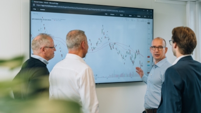 Our hedging department having a standing discussion in front of tv showcasing graph on electricity prices