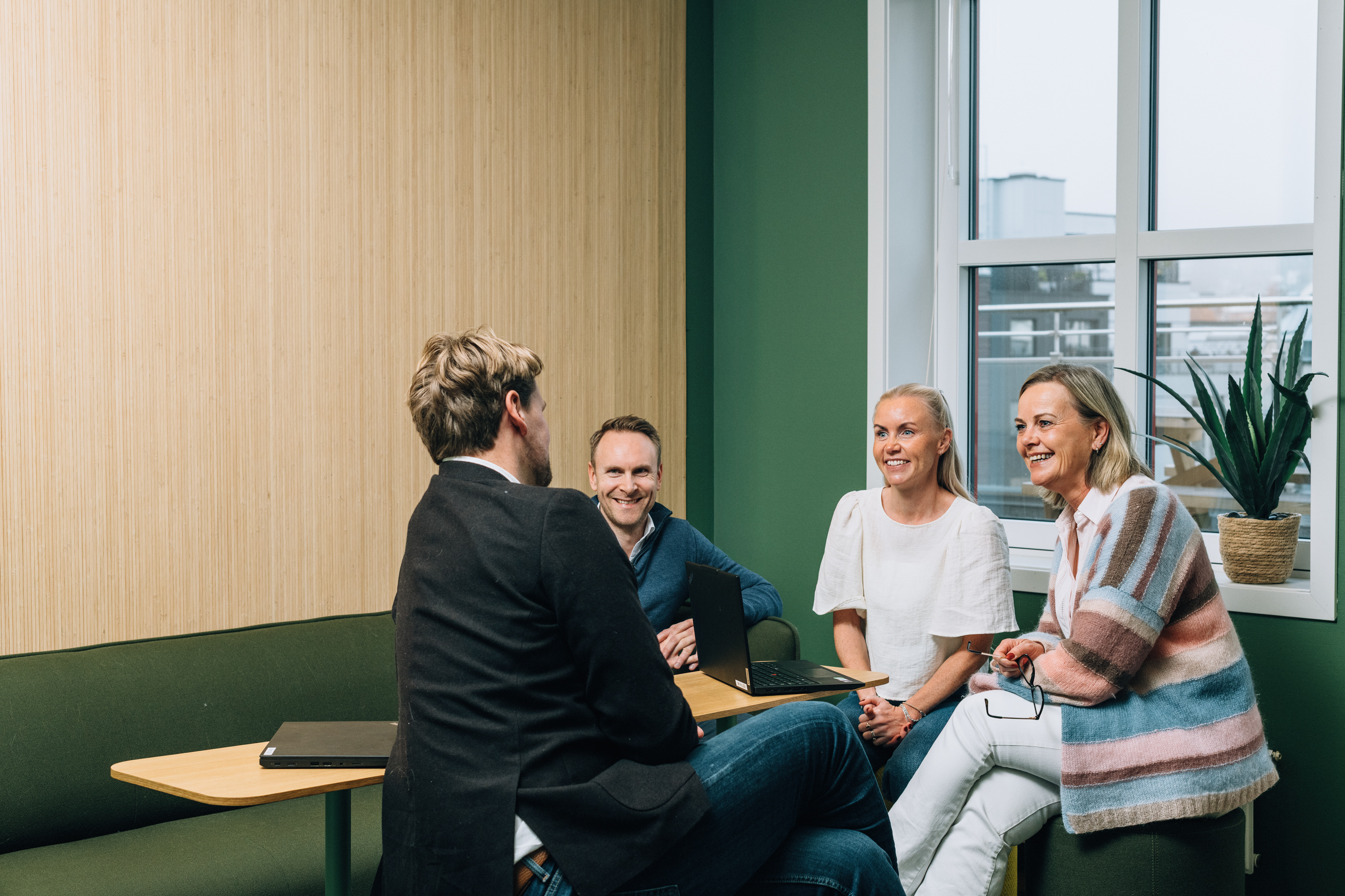 Four employees, two women and two men, gathered around a laptop in an inviting meeting room