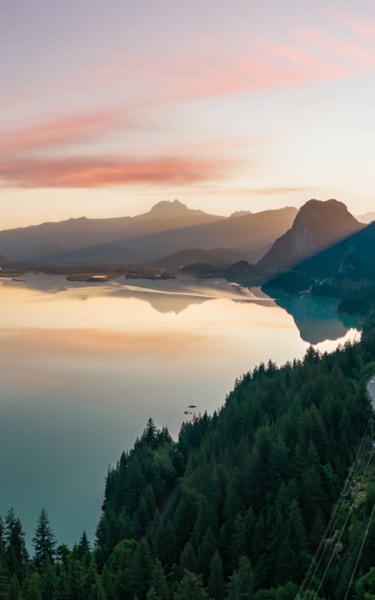 A scenic nature photo with a road running along mountains on the right side, and a big lake and mountains in the distance on the left